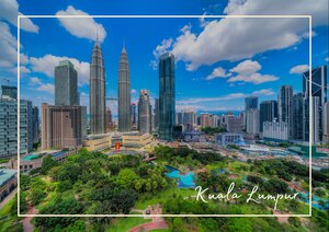Die Kuala Lumpur Skyline erhebt sich mit ihren modernen Hochhäusern und den markanten Türmen der Stadt über einer grünen Parkanlage. Zwischen den Wolkenkratzern und dem dichten Stadtbild setzt die Vegetation im Vordergrund einen auffälligen Kontrast. Der blaue Himmel und die weißen Wolken lassen die Architektur klar und weitläufig wirken.