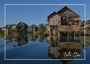 Am Inle-See stehen die hölzernen Häuser dicht am Wasser und spiegeln sich in der ruhigen Oberfläche. Die schmalen Pfähle, auf denen die Gebäude stehen, und die klare Spiegelung verleihen der Szene eine besondere Leichtigkeit.