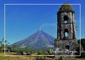 Vor dem Mount Mayon in Albay, Philippinen steht ein alter Steinturm, der das Bild im Vordergrund prägt. Der Vulkan erhebt sich im Hintergrund unter einem klaren blauen Himmel, wodurch die Szenerie eine eindrucksvolle und zugleich historische Kulisse bekommt.