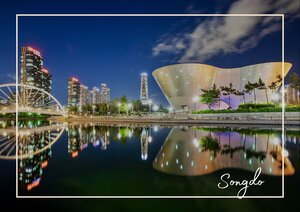 In der bekannten Smart City in Südkorea spiegelt sich die moderne Skyline ruhig im Wasser, während die große, schalenförmige Architektur sich hell vom dunklen Himmel abhebt und der ganzen Szene einen futuristischen Charakter gibt.