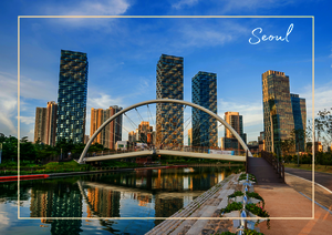 In Seoul verbindet die Szene eine elegante Fußgängerbrücke mit modernen Hochhäusern und einem ruhigen Wasserlauf, der die Architektur klar widerspiegelt. Die grünen Uferbereiche, der geschwungene Bogen der Brücke und die hellen Gebäude im Hintergrund geben dem Bild eine offene, klare und sehr städtische Wirkung.