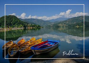 In Pokhara, Nepal liegen mehrere farbige Boote ruhig auf dem spiegelglatten See, während sich die grünen Hügel und der weite Himmel im Wasser widerspiegeln. Die Landschaft wirkt dadurch friedlich, klar und fast malerisch.